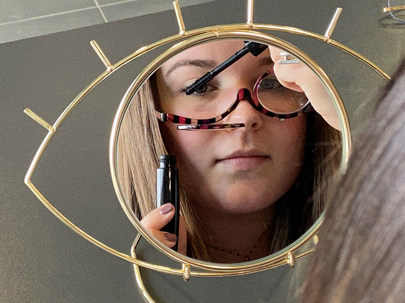 une jeune femme en train de sem maquiller avec des lunettes de maquillage en utilisant le miroir de table en forme d'oeil